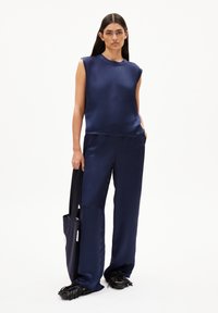 Navy satin sleeveless top paired with wide-leg navy trousers and a black tote bag with a strap. Detailed fringe shoes complete the look.