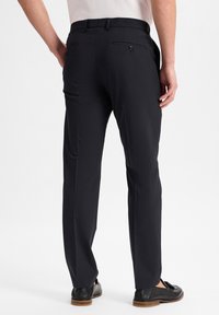 Dunkelblaue Hose mit taillierter Passform, glatter Textur, Gesäßtaschen mit Knöpfen und kombiniert mit schwarzen Schuhen.