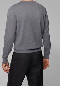 Grauer Pullover mit langen Ärmeln und Rundhalsausschnitt, aus weichem Stoff. Figurnahe Passform mit gerippten Bündchen und Saum, kombiniert mit schwarzer, maßgeschneiderter Hose.