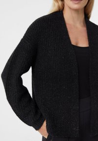 Czarny dzianinowy kardigan o luźnym kroju, z prążkowaną teksturą, otwartym przodem i długimi rękawami. Bez zapięć, zestawiony z czarną bluzką pod spodem.
