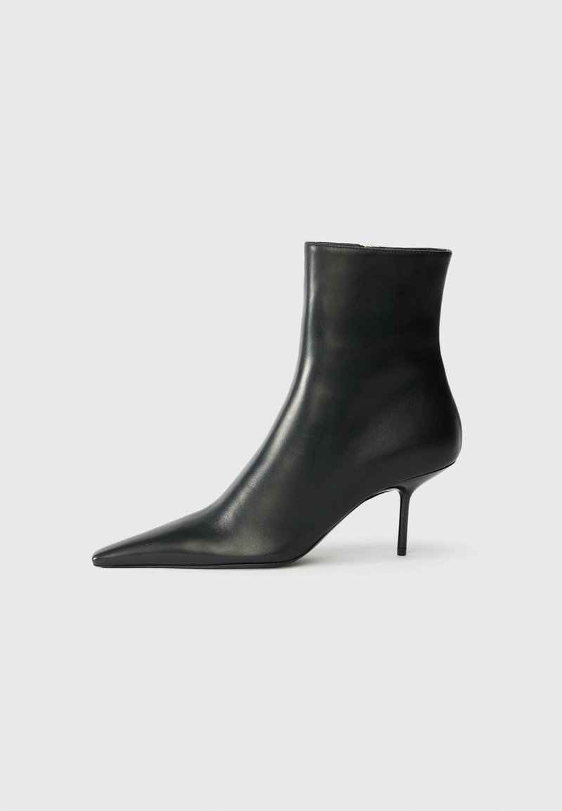 Bota de cuero negra hasta el tobillo con punta afilada y tacón de aguja delgado. Textura suave y diseño minimalista, con cierre de cremallera en la parte posterior.