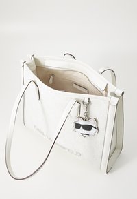 White tote bag made of synthetic material featuring a logo pattern, two handles, an interior zipper pocket, and a cat-shaped keychain.