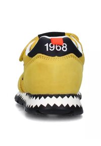 Sneaker in suede gialla con una suola zigzag nera e bianca, caratterizzata da un'etichetta rossa prominente e la scritta "1968" stampata sul tallone.