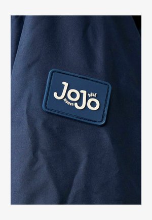 Torbica tamnoplave boje s teksturiranim, pravokutnim etiketom u plavoj boji s bijelim utisnutim tekstom "JoJo maman bébé." Glatkoga materijala, minimalističkog dizajna.