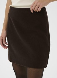 Jupe en laine marron avec une légère forme en A, présentant une fermeture éclair sur le côté et une texture lisse, associée à des collants noirs transparents.