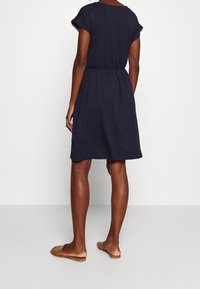 Granatowa sukienka na krótki rękaw z elastycznym pasem i ażurowymi akcentami na rękawach. Miękka, lekka tkanina w luźnym kroju.