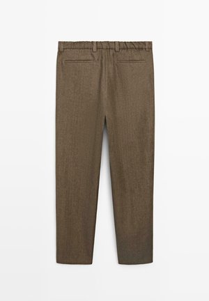 Brązowe, dopasowane spodnie z elastycznym pasem, szlufkami na pasek i dwoma tylnymi kieszeniami w listwą, pokazane od tyłu na białym tle.