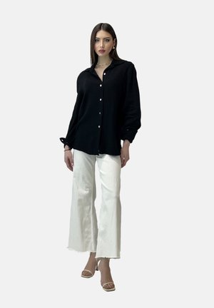 Camisa negra de botones con una tela texturada, mangas largas y botones perlados, combinada con pantalones amplios blancos y tacones nude.