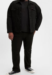 Černá džínová bunda s dvěma náprsními kapsami, v kombinaci s černým tričkem a černými džíny. Námořnické tenisky outfit doplňují.