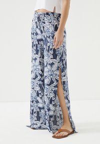 Maxipantalon met een marineblauw en witte bladerenpatroon. Voorzien van een trekkoord in de taille, zijsleuven en lichte stof. Gecombineerd met bruine sandalen.