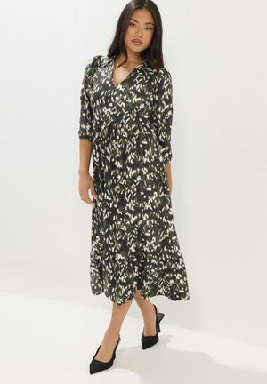 Mujer de pie vistiendo un vestido midi con estampado abstracto en blanco y negro, mangas tres cuartos y tacones negros de punta.