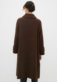 Cappotto di lana marrone con colletto ampio, maniche lunghe e silhouette dritta; presenta tasche laterali e una lunghezza media.