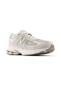 Baskets de sport beiges avec tige en maille et en daim, présentant une semelle blanche et de subtils accents gris. Conçues pour le confort et la stabilité.
