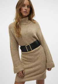 Abito maglione beige con collo alto, maniche lunghe e finitura testurizzata, cintrato in vita da una larga cintura nera con fibbia dorata.