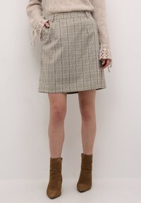 Beige ternet nederdel med lige snit, sidelommer og tekstureret stof. Sammen med brune ankelstøvler, hvilket giver et afslappet look.