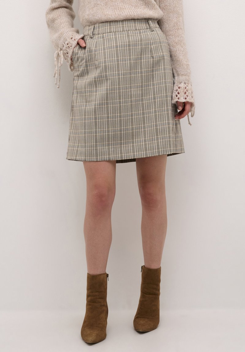 Beige ternet nederdel med lige snit, sidelommer og tekstureret stof. Sammen med brune ankelstøvler, hvilket giver et afslappet look.