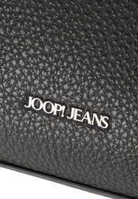Superficie in pelle nera testurizzata con il logo metallizzato argento "JOOP! JEANS" impresso al centro.