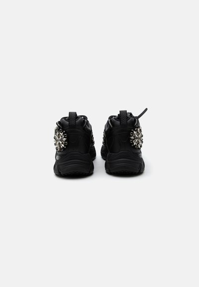 Ζευγάρι μαύρα sneakers που φαίνονται από πίσω με διακοσμητικά σε σχήμα λουλουδιού από στρας στις εξωτερικές πλευρές και λουράκια στα τακούνια.