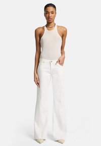 Witte wijde jeans en een beige geribbelde tanktop. De tanktop heeft een halternekontwerp, terwijl de jeans voorzakken en een hoge taille hebben.