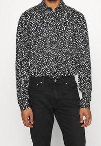 Camicia a maniche lunghe a righe bianche e nere con un design vorticoso. Abbinate a jeans di denim scuro.