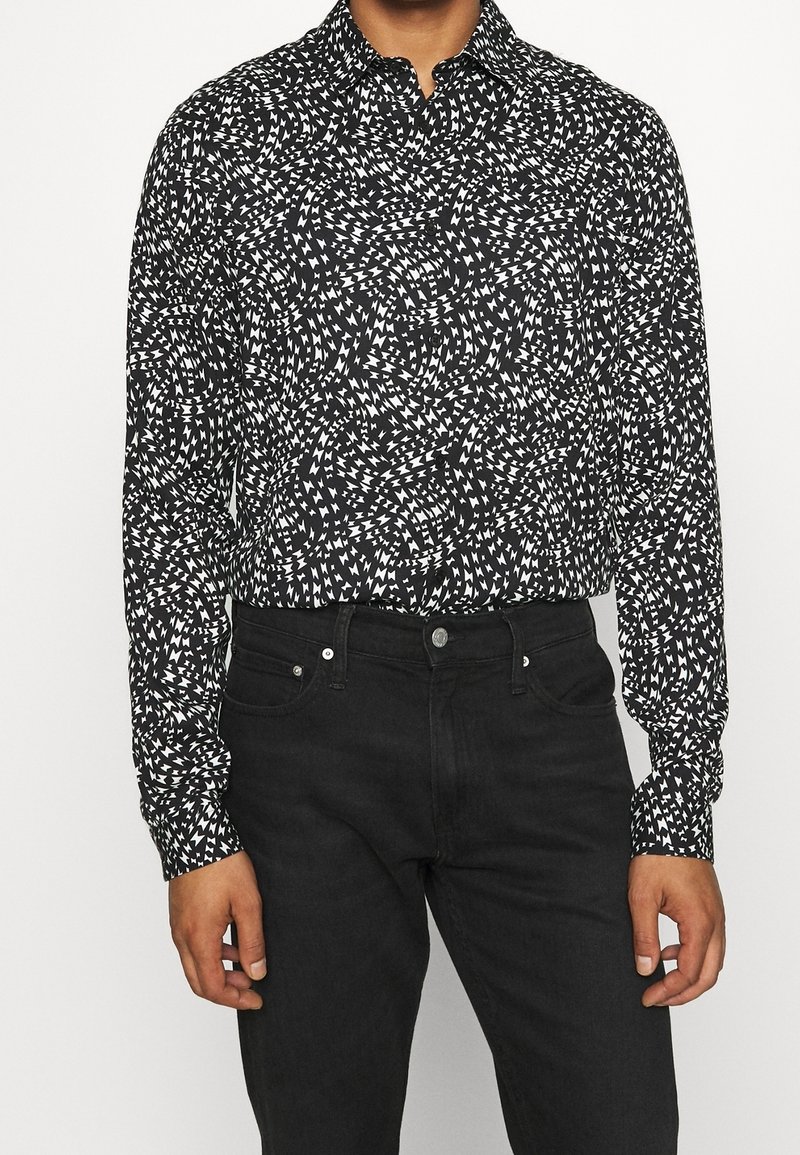 Camicia a maniche lunghe a righe bianche e nere con un design vorticoso. Abbinate a jeans di denim scuro.