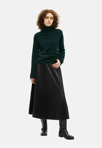 Mørkegrøn rullekravesweater parret med en sort plisseret midiskirt. Tekstureret stof, tætsiddende ved taljen, med glatte, blanke accenter.
