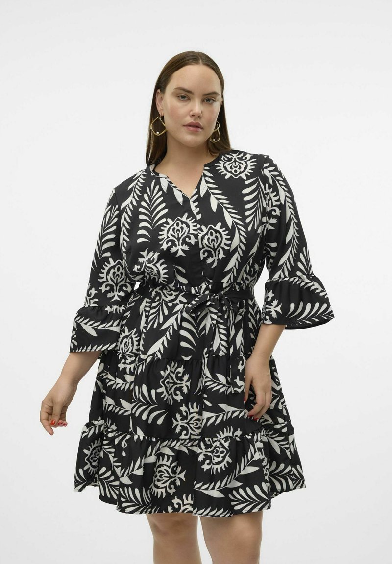 Robe à motifs floraux noir et blanc avec des volants superposés, décolleté en V et taille ceinturée. Fabriquée en tissu léger avec une texture lisse.