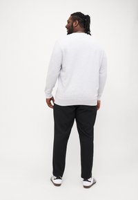 Grau gestrickter Pullover mit langen Ärmeln, rundem Hals und gerippten Bündchen, kombiniert mit schwarzen Hosen und weißen Turnschuhen. Rückansicht angezeigt.