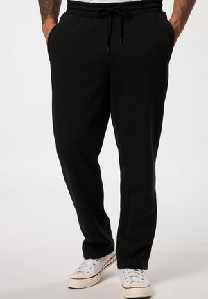 Sorte sweatpants med elastisk talje og snor, sidelommer og en tapered ben design. Båret med hvide sneakers.