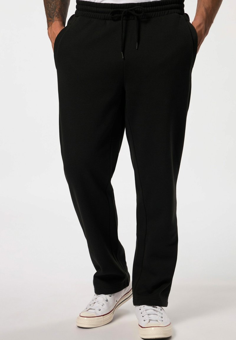 Zwarte sweatpants met een elastische tailleband en trekkoord, zijzakken en een tapered leg ontwerp. G gedragen met witte sneakers.