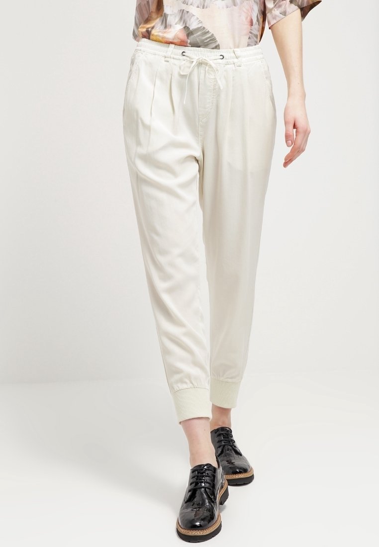 Ljust beige joggerbyxor med elastisk midjeband och muddar, tillverkade av ett slätt textilmaterial; har framfickor för en avslappnad passform.