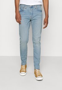 Ljusblå denimjeans med en figursydd design, femficksstil och subtila blekningar. Kombinerade med gula sneakers med vita sulor.
