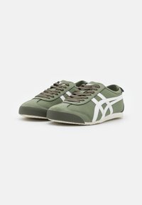 Zapatillas verdes con acentos blancos, que presentan una parte superior de tejido suave, punta redonda y suela plana de goma. Cordoneras en un tono oliva a juego.