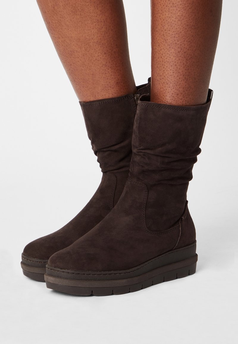 Braune Wildleder-Stiefeletten mit gerafftem Design, flacher Plateausohle und seitlichem Reißverschluss. Glatte Textur und minimale Nähdetails.