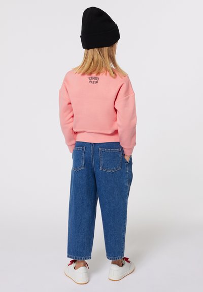 Sweatshirt rose à col rond avec un détail brodé, associé à un jean en denim ample avec poches arrières, et des baskets blanches.