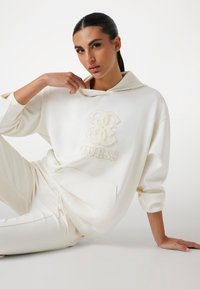 Witte hoodie met een geborduurd "GUESS" logo, met een relaxte pasvorm, lange mouwen en een kangoeroezak. Zacht, gestructureerd materiaal.