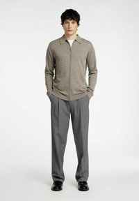 Svetlo siva zip-up jopica s ravnim ovratnikom, v kompletu z ohlapnimi sivimi hlačami. Ima gladko teksturo in prilegajoče manšete, nosi se z črnimi čevlji.