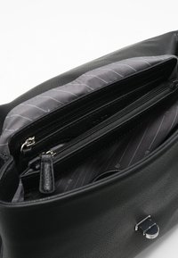 Sac en cuir noir avec doublure à rayures grises, comportant deux compartiments zippés et un accent en métal argenté. Texture lisse sur l'ensemble.