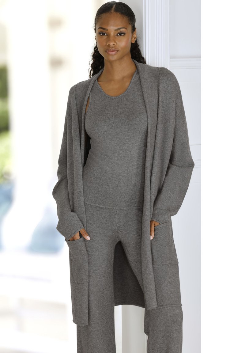 Pilkas megztinis su atvira priekiu, ilgomis rankovėmis ir šoninėmis kišenėmis. Nešiojamas virš suderinto palaidinės ir kelnių, turintis glotnią tekstūrą.