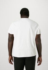 Camiseta blanca de algodón con mangas cortas, corte relajado y escote redondeado, combinada con jeans oscuros. Sin logotipos ni patrones visibles.