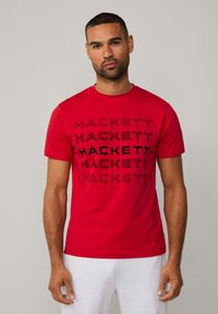 Camiseta de algodón roja con el texto repetido "HACKETT" en negro, diseño de cuello redondo, mangas cortas y una textura suave.