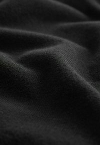 Černá pletenina s hladkou texturou, ukazující záhyby a jemný lesk, zdůrazňující její měkkost a splývavost.