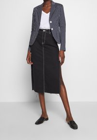 Blazer rayé bleu marine et blanc, t-shirt blanc, jupe crayon en denim noire avec des coutures contrastées, fentes sur les côtés et chaussures plates noires.