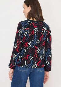 Langærmet bluse i et sort stof med et livligt zigzag-mønster i rød, blå og hvid. Rund halsudskæring og afslappet pasform.