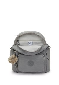 Sac à dos Kipling gris avec une poche avant, compartiment principal ouvert montrant une poche zippée à l'intérieur et un porte-clés en forme de singe en peluche attaché.