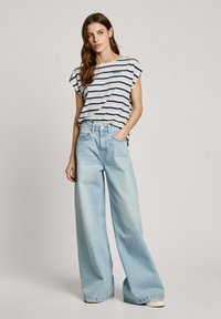 Striped short-sleeve top with wide sleeves, paired with light blue wide-leg jeans featuring a high waist and contrasting stitching.