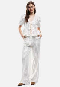 Top peplo bianco a righe con maniche a palloncino corte e chiusura a fiocco, abbinato a pantaloni larghi bianchi a righe e scarpe flat marroni.