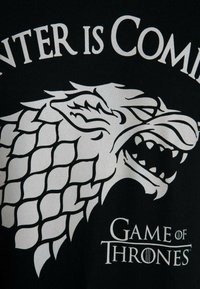 Black t-shirt featuring a large, white direwolf graphic with a textured scale pattern. Text reads "Winter is Coming" and "Game of Thrones."