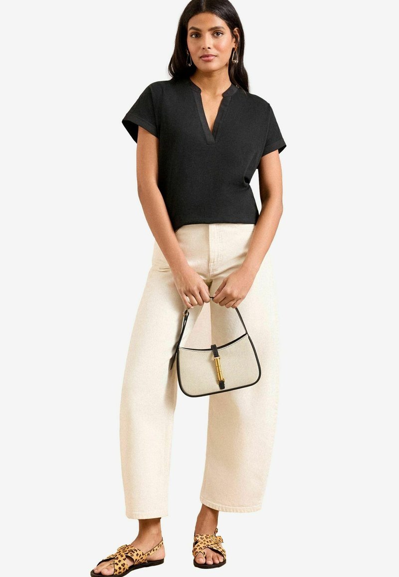 Melns īsām piedurknēm tops ar V veida kakla izgriezumu, krēmkrāsas plaša kāju bikses, leopardu raksta sandales un maza krēmkrāsas rokassoma ar melniem akcentiem.