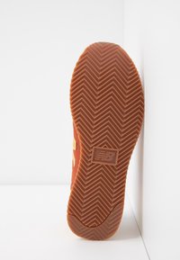 Semelle d'une basket New Balance marron avec un motif en chevrons et un logo carré au centre sur fond blanc.